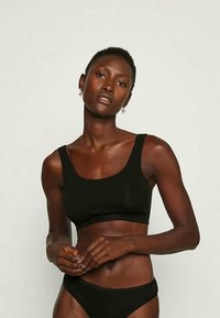 Juodas trumpas viršus su kvadratiniu iškirpimu ir plačiomis petnešėlėmis, derinamas su atitinkamais bikini apatiniais. Lygus paviršius, minimalizmo dizainas.