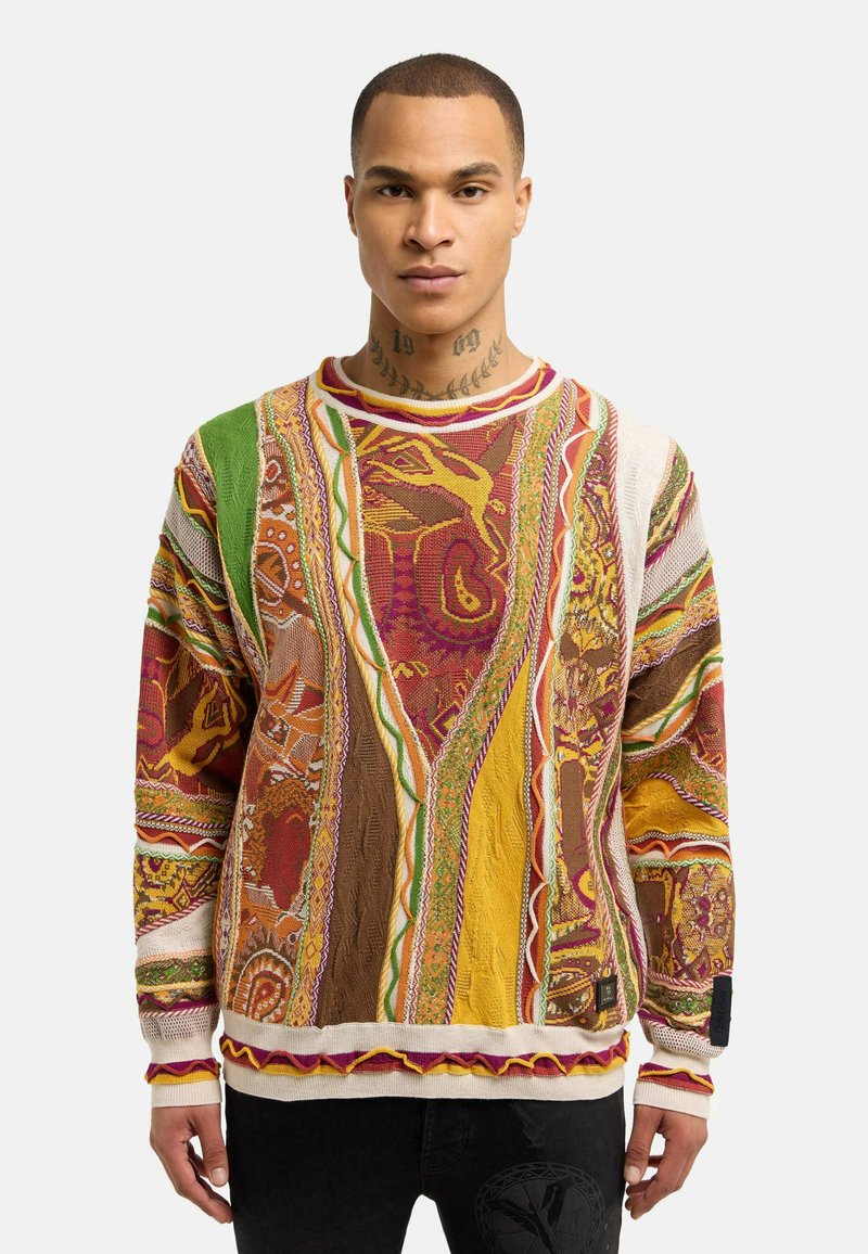 Pull en tricot coloré avec des motifs complexes en rouge, jaune et vert. Caractéristiques de tissu texturé, col rond et finitions contrastées.