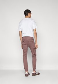 Lichte witte katoenen t-shirt en getailleerde cargo-broeken in gedempt mauve met zijzakken, elastische manchetten en bruine suède sneakers.