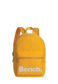 Sac à dos en nylon jaune avec une forme arrondie, muni d'une poche avant zippée et du logo « Bench. » imprimé en blanc. Comprend des bretelles rembourrées.