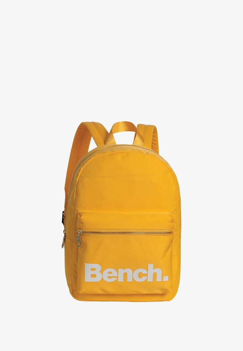 Sac à dos en nylon jaune avec une forme arrondie, muni d'une poche avant zippée et du logo « Bench. » imprimé en blanc. Comprend des bretelles rembourrées.