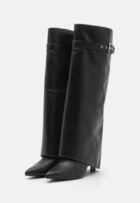 Botas de tobillo de cuero negro con puntera puntiaguda, que presentan un corte alto y estructurado y un acento de hebilla delgada en la parte superior.