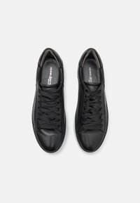 Baskets en cuir noir avec une texture lisse, dotées de lacets traditionnels, d'un bout arrondi et d'un design minimaliste. Semelle en caoutchouc blanc.