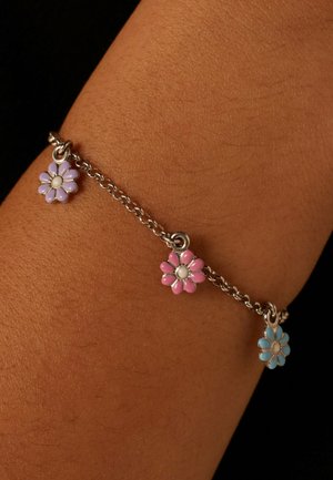 Silberne Kettenarmband mit drei Blumenanhängern in Lila, Pink und Blau mit weißen Mittelpunkten, vor einem strukturierten Hauthintergrund.