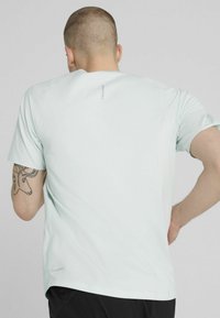 Lys mintgrøn kortærmet t-shirt lavet af blødt stof, med et subtilt design på ryggen og en afslappet pasform.