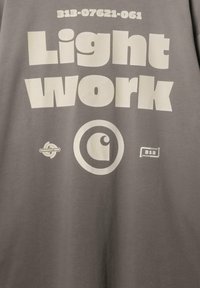 Szara bawełniana koszulka z dużym białym napisem: "Light Work" oraz różnymi logo. Szczególne grafiki obejmują okrągły wzór oraz liczby.