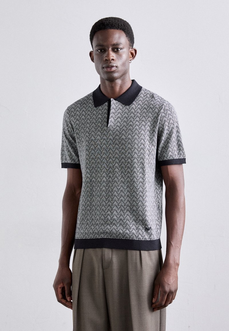 Polo à manches courtes dans un motif zigzag texturé gris et noir, avec un col et des poignets noirs, un ourlet droit et une coupe ajustée.