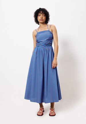 Blauw en rood gestreepte jurk met een aansluitend lijfje, spaghettibandjes en een vloeiende, knielange rok. Gecombineerd met rode sandaaltjes met bandjes.