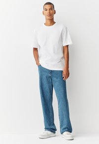 Tricou alb din bumbac, asortat cu blugi albaștri cu croială lejeră. Modelul poartă adidași albi; design casual cu siluetă cu picior drept.