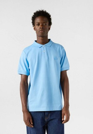 Polo de color azul claro hecho de algodón, con cuello tipo polo y tapeta de tres botones. Manga corta y sutil detalle del logo en el pecho.