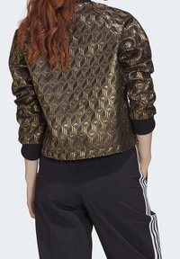 Černá bomber bunda se zlatým geometrickým vzorem, s ribbed manžetami a lemem. Vyrobena z lesklého materiálu s jemným leskem.