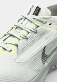 Les chaussures Nike Pegasus Trail 5 disposent d'un dessus léger gris avec des motifs texturés, des accents jaune fluo et un logo swoosh noir. Traitement Gore-Tex appliqué.
