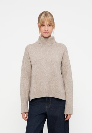 Bežna pletena turtleneck pulover s sproščenim krojem, rebrastimi manšeti in bočnimi razporki, v kombinaciji s temnimi kavbojkami. Mehka tekstura, lahek material.