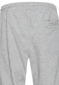 Grå joggebukser med elastisk midje, myk tekstur og en enkelt baklomme med horisontal åpning.