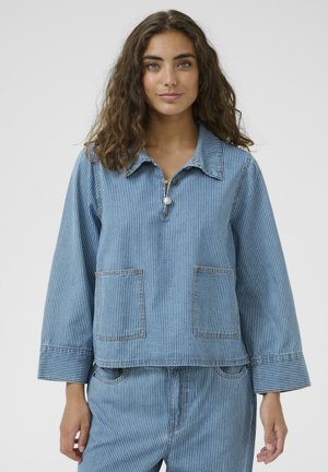 Svetlomodrý látkový top s vertikálnymi bielymi pruhmi, s golierovým výstrihom, dvoma prednými vreckami a širokými rukávmi.