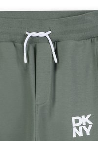 Groene sweatpants met een trekkoord met witte uiteinden en een wit DKNY-logo op het onderste rechterbeen. Gladde stof met een casual ontwerp.
