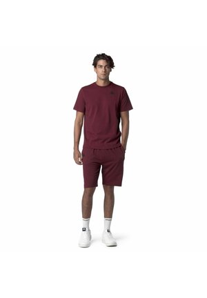 T-shirt bordeaux a maniche corte abbinata a pantaloncini dello stesso colore, realizzati in materiale morbido. Presenta un piccolo logo nero sul petto.