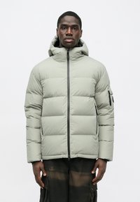 Vaahtomuovilla vuorattu harmaanvihreä takki, jossa on vetoketju edessä ja huppu. Takissa on sivutasku ja ommellut paneelit eristyksen lisäämiseksi. Pintakäsittely on sileä ja mattapintainen.