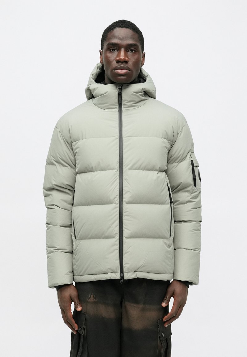 Vaahtomuovilla vuorattu harmaanvihreä takki, jossa on vetoketju edessä ja huppu. Takissa on sivutasku ja ommellut paneelit eristyksen lisäämiseksi. Pintakäsittely on sileä ja mattapintainen.