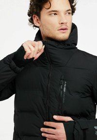 Schwarze Steppjacke mit hohem Kragen, Reißverschluss vorne und elastischen Bündchen. Verfügt über eine kleine Brusttasche und eine glatte, matte Textur.