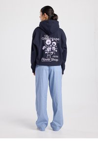 Sweat à capuche bleu marine avec un motif floral et un texte au dos, associé à un pantalon bleu clair à fines rayures, offrant une coupe décontractée et un tissu doux.