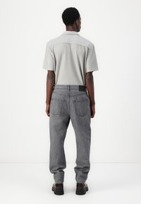 Grå kortermet polo skjorte med ribbestruktur, sammen med høyt liv lysegrå jeans og svarte kraftige sko. Bakside.