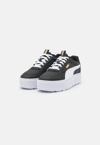 Baskets plateforme noires et blanches avec des semelles épaisses blanches, des lacets blancs et un logo Puma doré sur la languette et sur le côté.