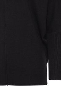 Tela negra de punto con costura visible y bordes de puño y dobladillo acanalados, mostrando la textura y detalles de la confección de la prenda.