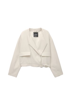 Ingeperkt beige blazer met een reverskraag, twee voorkruiken en een ronde gespdetail aan de zijkant. Gladde stof met een minimale textuur.