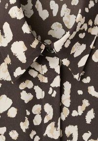 Rjava srajca iz tkanine z leopardjim vzorcem v krem in bež barvi, s koničastim ovratnikom in detajli zapenjanja na gumbe.