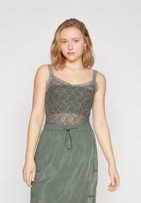 Grå blonder tanktop med intrikat blomsterdesign og justerbare blonderstropper, båret med en matchende grønn skjørt med snor i livet.
