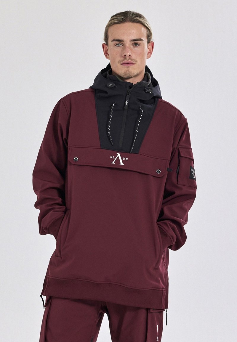 Mørkerød sweatshirt med sort hætte, frontlomme og snøre. Har et logo på brystet og et sidepatch, lavet af blødt materiale.