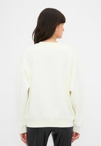 Svetle krémová mikina s volným střihem, kleslými rameny a žebrovanými manžetami. Dokončena měkkou texturou a pohodlným pasem.