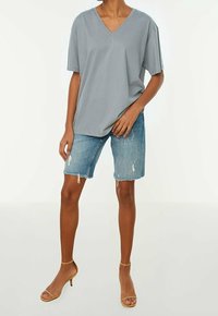 T-shirt grigio chiaro a V con maniche corte, abbinato a pantaloni shorts in denim strappati e sandali con tacco nudo. Stile semplice e vestibilità rilassata.