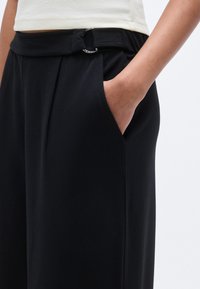 Μαύρο παντελόνι με ραφή, σχεδιασμένο με πιέτες, διαθέτει θηλιά για ζώνη με ασημένιο δαχτυλίδι και πλαϊνές τσέπες. Ελαφρύ και λείο ύφασμα.