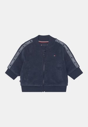 Granatowa bluza polarowa na suwak z prążkowanym kołnierzem i mankietami, z oznaczeniem Tommy Hilfiger na rękawach i małym logo na piersi.