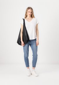 Hvit v-hals t-skjorte, blå jeans og hvite joggesko. Svart lær skulderveske med teksturert overflate, båret på venstre skuldre.