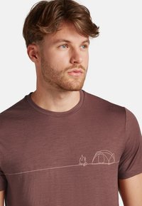 Braunes Kurzarm-T-Shirt aus weichem Stoff mit minimalistischem weißen Linien-Graphic einer Camping-Szene, die ein Zelt und ein Lagerfeuer zeigt.