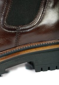 Gros plan d'une botte en cuir brun foncé avec un panneau latéral élastique noir, des coutures détaillées, une semelle superposée et une semelle extérieure en caoutchouc noir robuste.