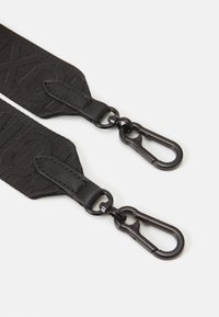 Sangle noire ajustable en tissu texturé avec quincaillerie noire contrastante. Dotée de clips métalliques pour fixation à chaque extrémité.
