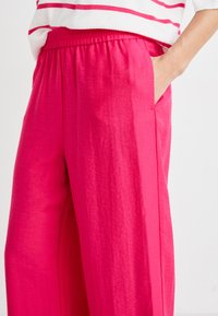 Pink, lightweight, loose-fitting trousers with an elastic waistband and side pockets; smooth texture with a subtle sheen.