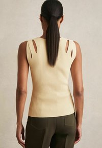 Canotta beige a maglia a coste con spalle scoperte, abbinata a pantaloni verde oliva. Presenta una silhouette aderente e una texture liscia.