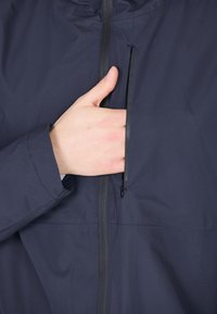 Mörkblå jacka med en ficka på bröstet som stängs med dragkedja. Tyget är slätt med en subtil struktur och har en ståkrage samt elastiska ärmmuddar.