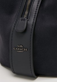 Granatowa torebka z zamszu z paskiem ze skóry, złotym suwakiem oraz metalową etykietą z logo "COACH" i "NEW YORK".