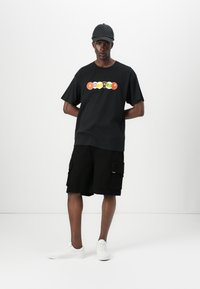 Black t-shirt with colorful circular graphic, paired with black cargo shorts featuring pockets. White sneakers complete the outfit.