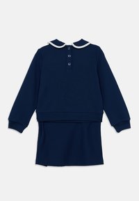 Διμερές σύνολο σε ναυτικό μπλε χρώμα, που αποτελείται από μπλούζα με μακρύ μανίκι και λευκή γιακά, και φούστα σετ με ίσιο τελείωμα.