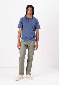 Blue short-sleeve shirt with two buttons, paired with olive green straight-leg pants and light-colored sneakers. Simple modern design.