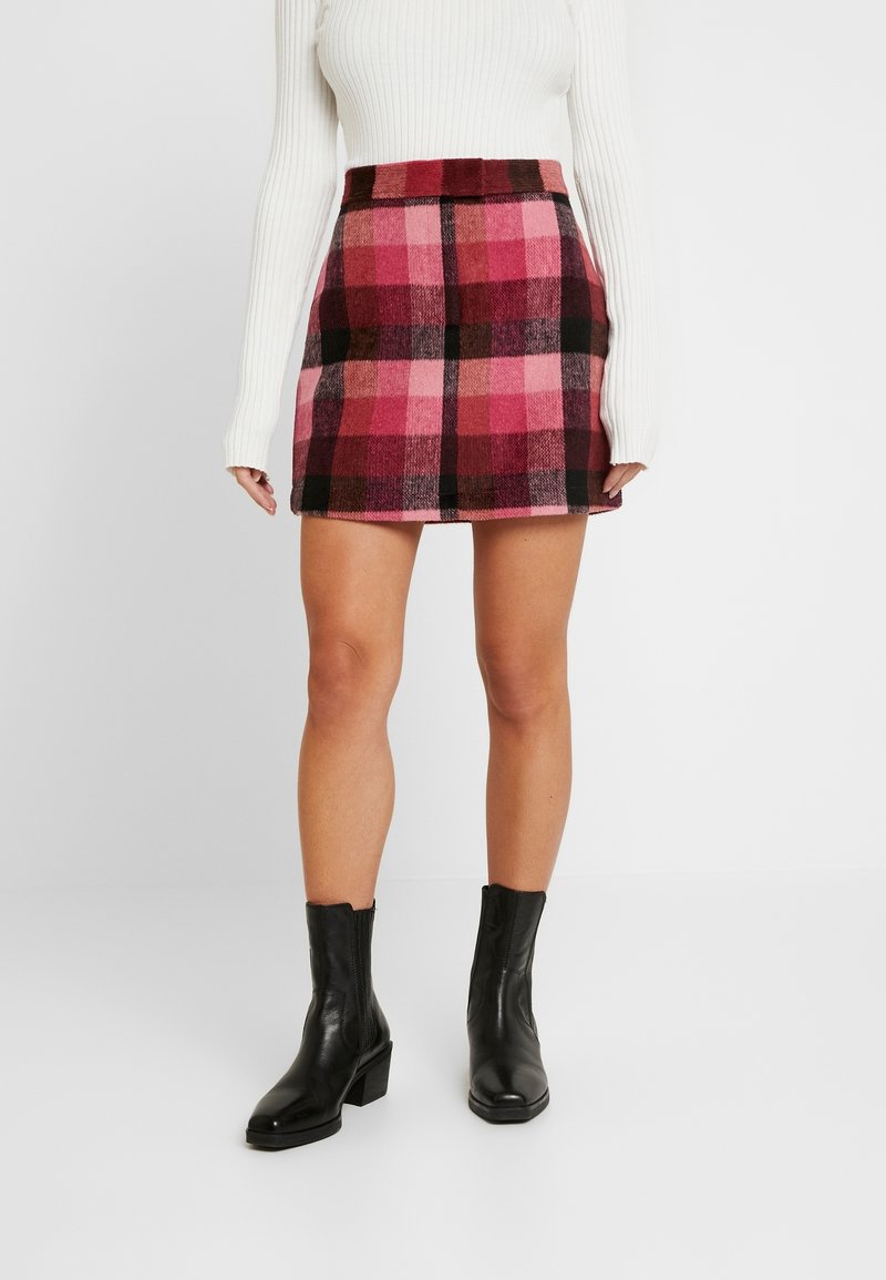 Plaid mini skirt in pink, black, and red hues with a smooth texture, featuring a fitted waist and a straight cut design, paired with black boots.