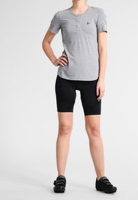 Camiseta deportiva gris de manga corta con diseño henley y pequeño logo de acento, combinada con pantalones cortos de compresión negros y zapatos de ciclismo.