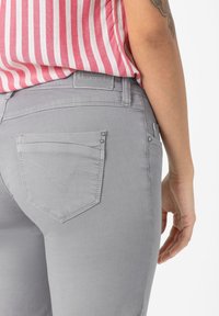 Gray denim jeans with a fitted design, two back pockets featuring decorative stitching, and subtle silver hardware on the pocket edges.